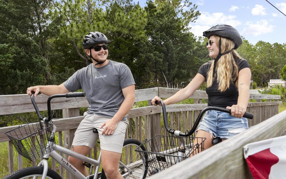Attractive young couple wearing helmets bicycles across a wooden bridge in Salvo on Hatteras Island