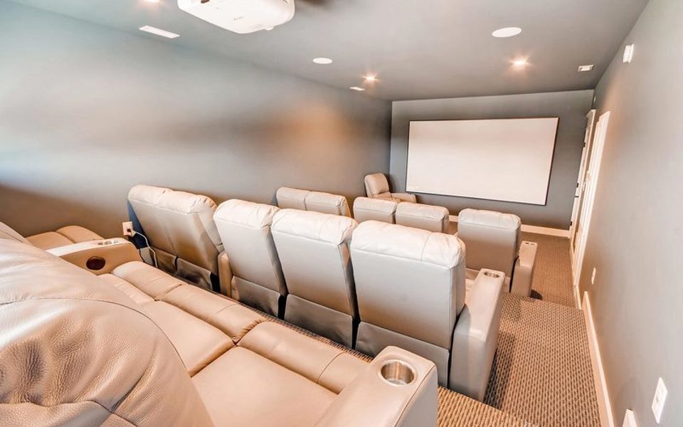 Three rows of tan leather reclining theater seats face a large screen in the Theater Room of this premier vacation home