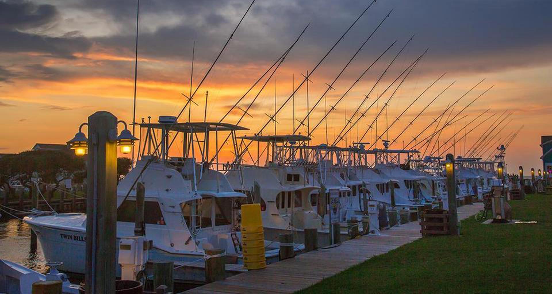 Row of Hatteras-based off-shore charter fishing boats line the dock at Teach's Lair Marina under an orange pre-dawn sky