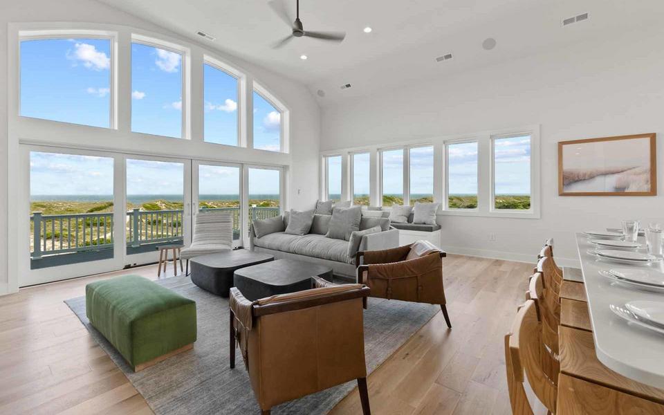 A grid of eight large picture windows look out from an expansive great room in a vacation home to blue skies outside
