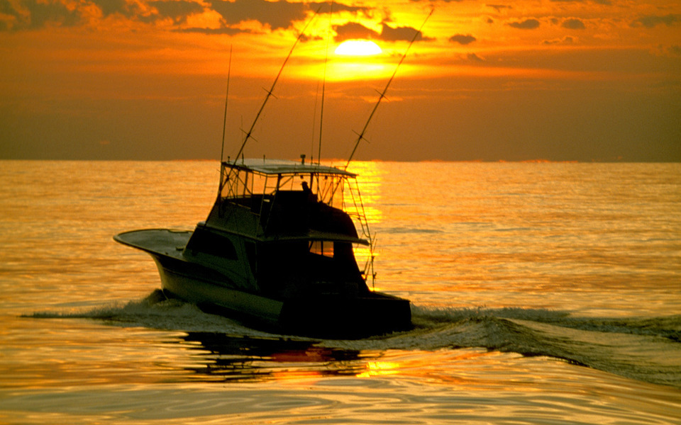 Silhouette of a charter fishing boat framed by an orange sunset over the ocean reflecting on the water