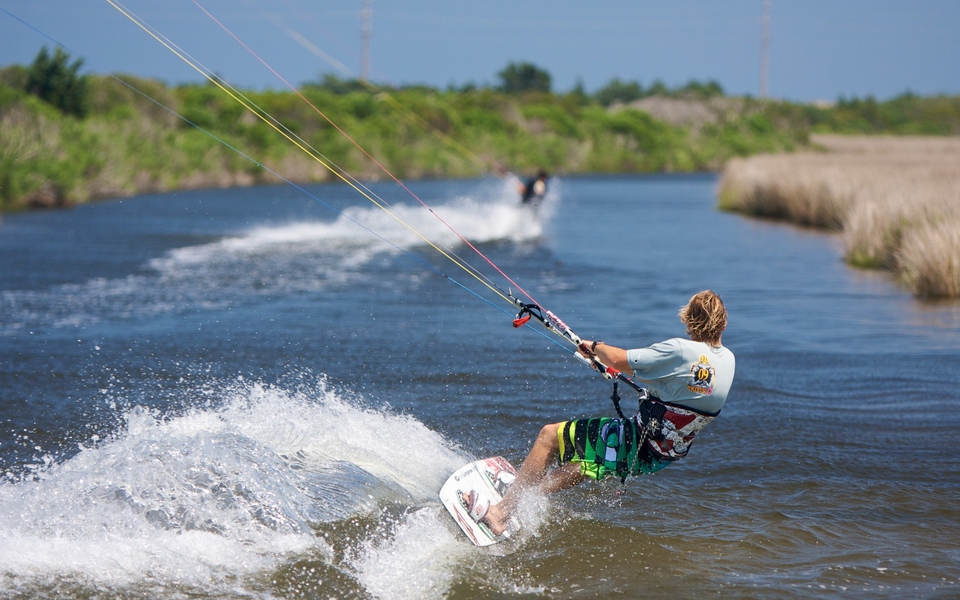 View from behind two kiteboarders carving down a narrow cut along the edge of the Pamlico Sound near Rodanthe