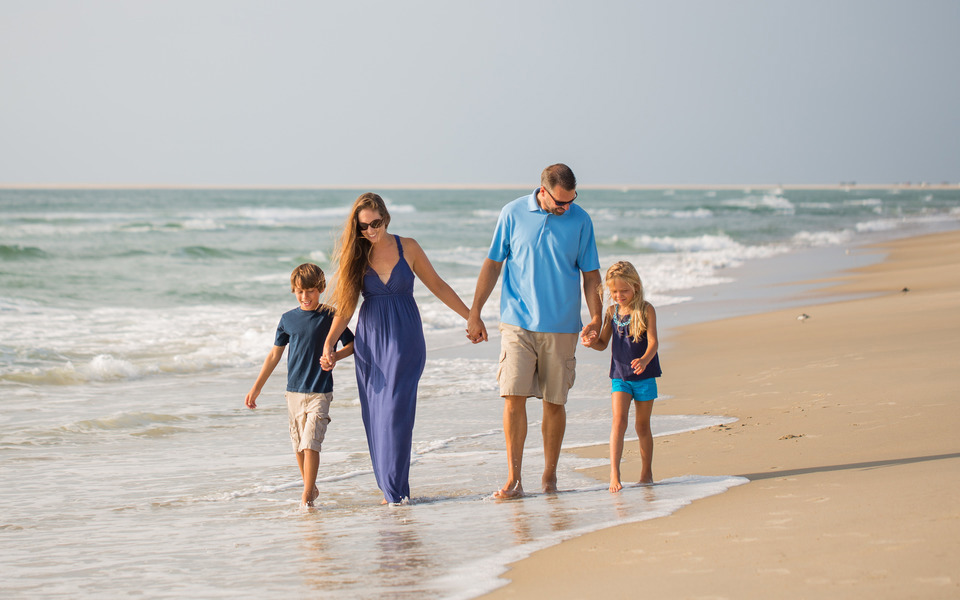 Family with adolescent kids walks in the gently lapping waves on the beach on the Outer Banks of North Carolina
