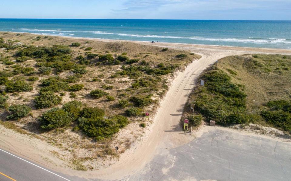 A sand access road leads to the beach and the ocean beyond in this drone shot from over a parking access near Route 12