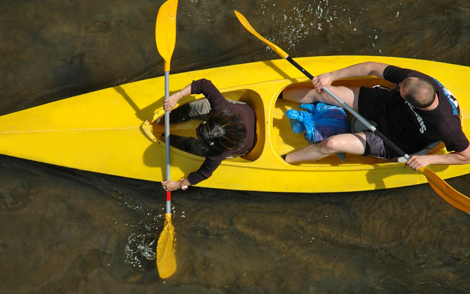 Bird's eye view of a couple in a bright yellow tandem kayak with yellow paddles from directly above the shallow sound