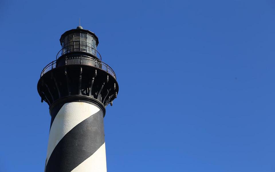 Daytime view looking up at just the top of the Cape Hatteras Lighthouse against a deep blue cloudless sky