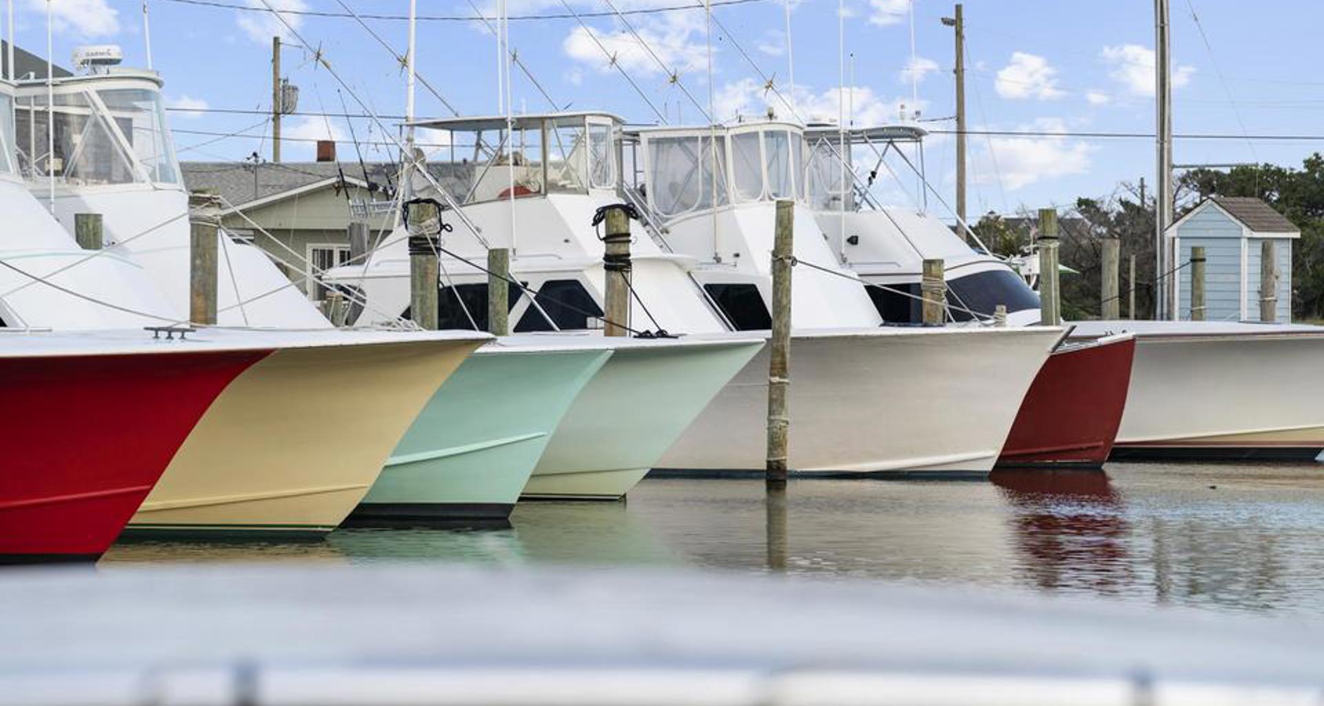 The colorful hulls of 7 charter fishing boats point out into the waters of the marina in Hatteras Village