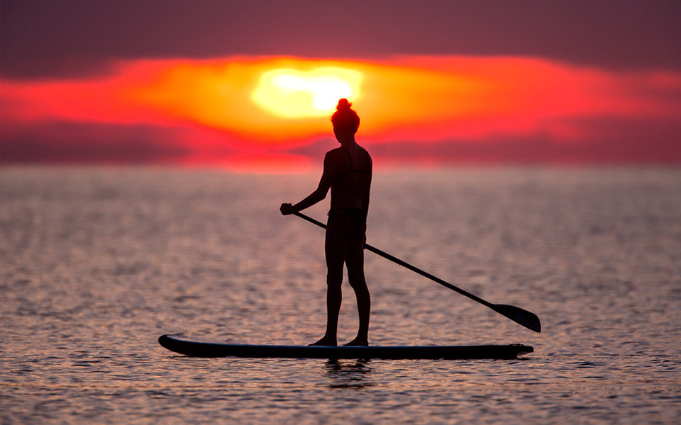 Silhouette of a woman holding a paddle on a paddle board on the Pamlico Sound at sunset. Pink and orange sky.