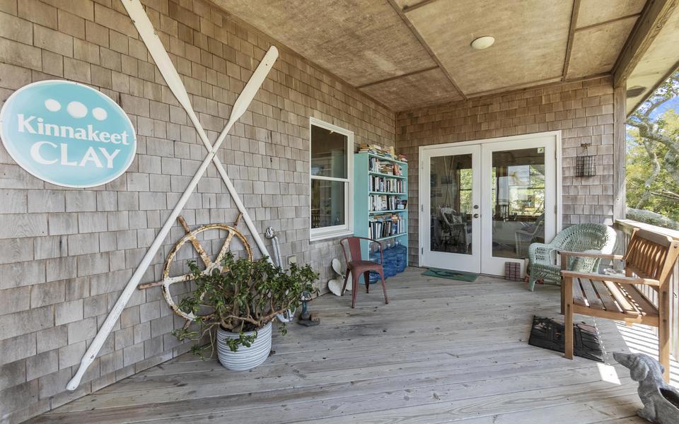 The covered front porch entrance to Kinnakeet Clay with crossed oars, a bench, and some potted plants.