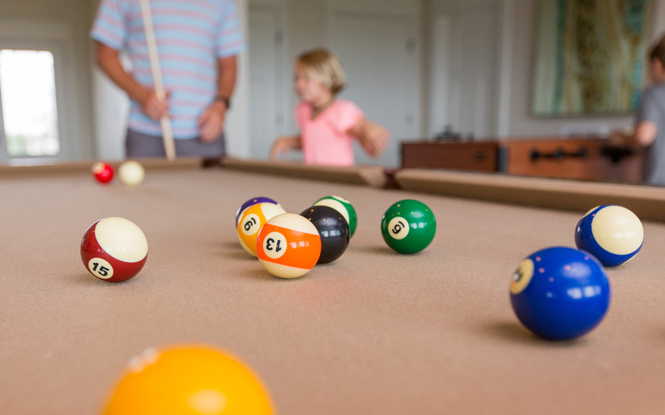 Billiard balls on a tan felted pool table in vacation home game room with a tween in the background