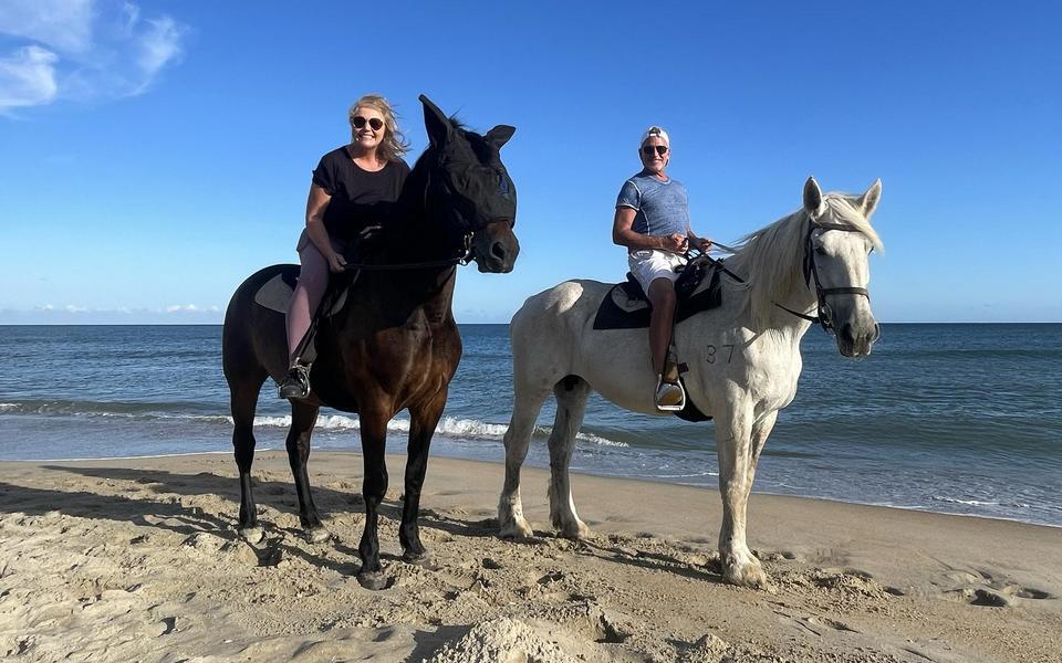 Couple poses on horseback in front of a calm ocean and a deep blue sky near Hatteras Village on the beach