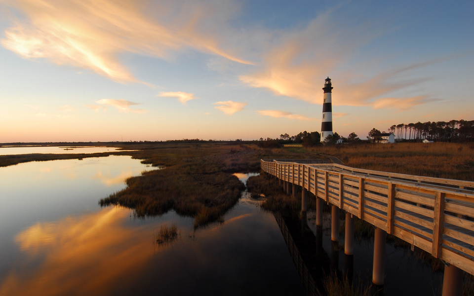 Wispy clouds glow post sunset and are reflected in glassy, sound waters near the Bodie Island Lighthouse and walkway