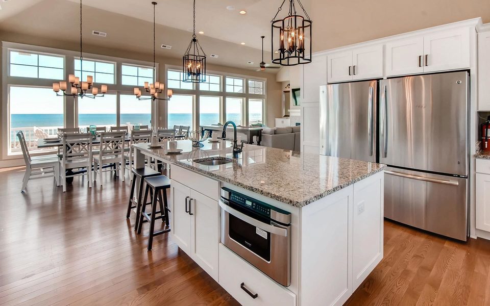 Modern kitchen with double fridges, a granite-topped island with a warming oven. Large dinning table with a wall of windows.