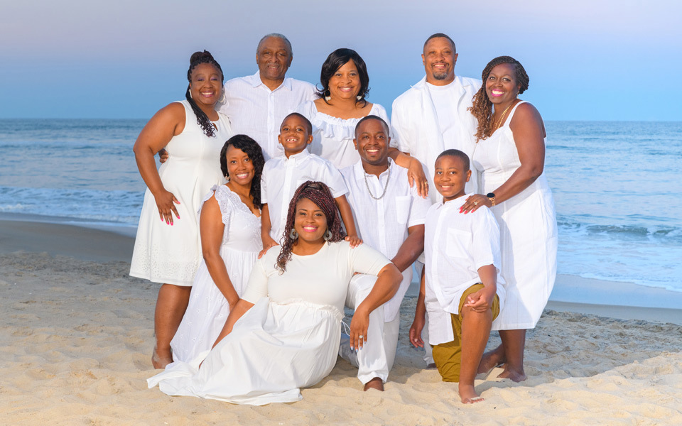Extended family of ten, all dressed in white, pose as a group on a Hatteras Island beach at twilight