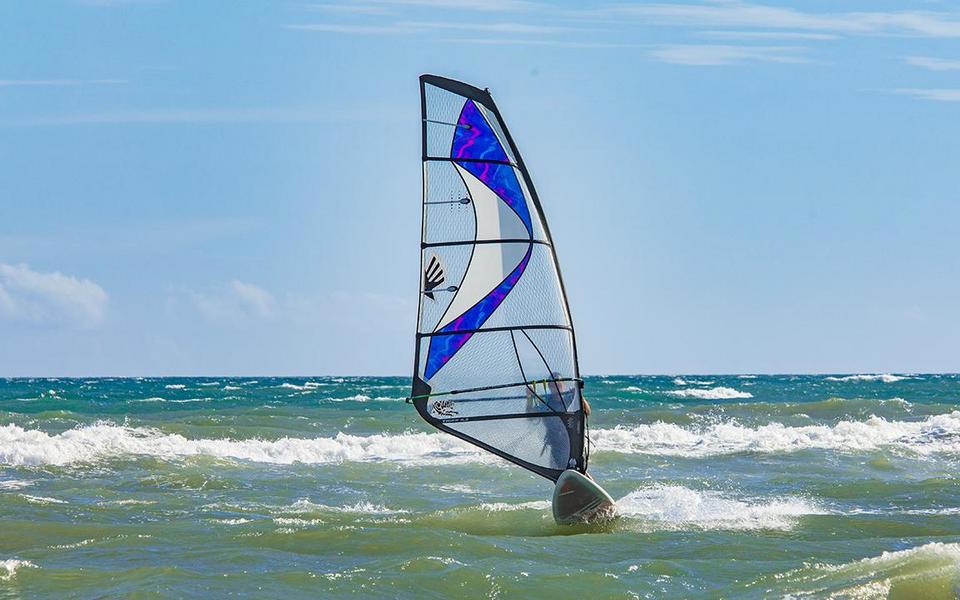 Windsurfer rides the wind toward the viewer with incoming waves on the ocean