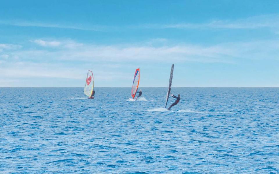 Three windsurfers sail off toward the horizons on a beautiful blue sky day