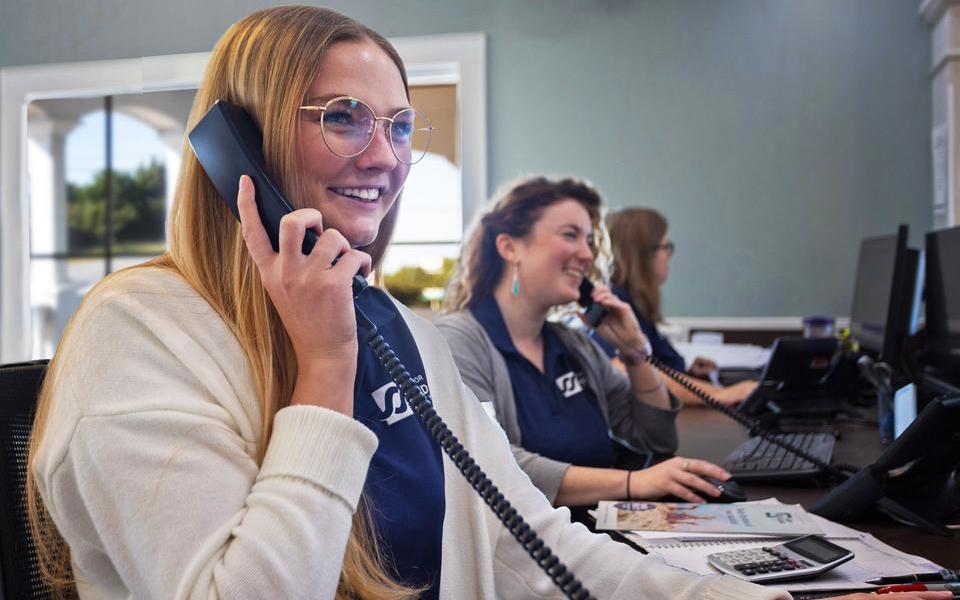 Three employees smile doing their jobs as vacation specialists in the Salvo office of Surf or Sound Realty