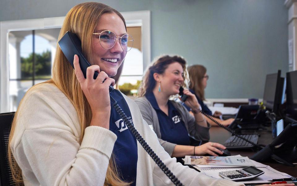 Three employees smile doing their jobs on phones as vacation specialists in the Salvo office of Surf or Sound Realty