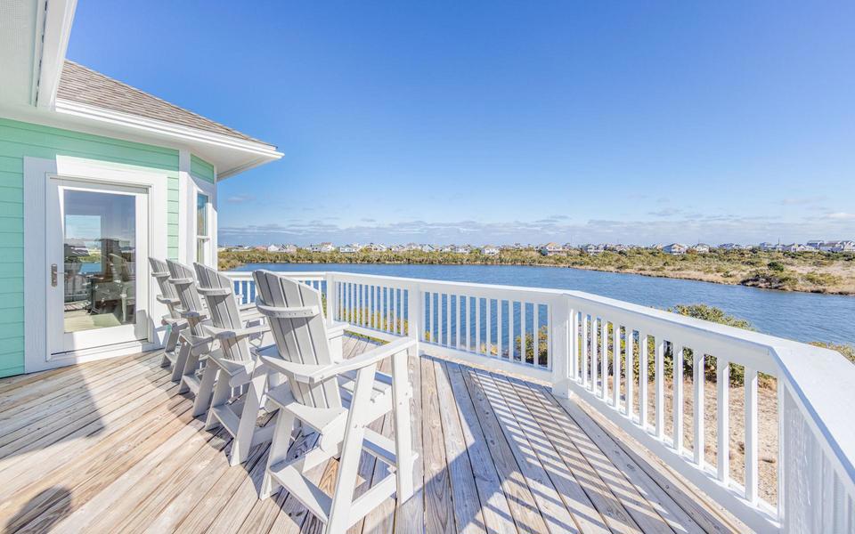 Four white Adirondack chairs on a vacation home deck overlook a spring scene along a canal on Hatteras Island