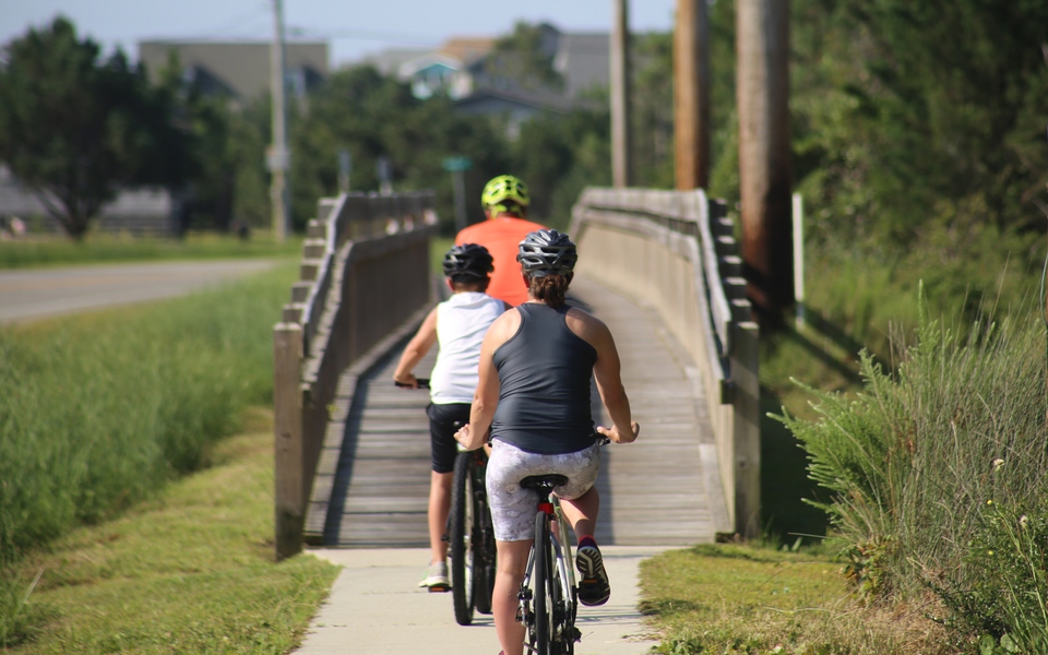 Family of three cyclists bike away toward a wooden multi-use bridge in Salvo heading south