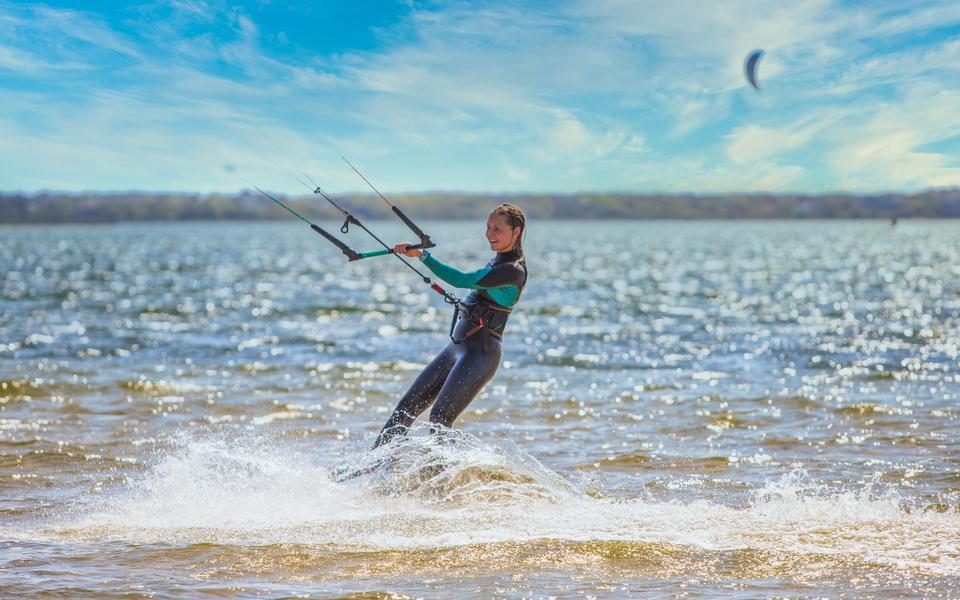 Kiteboarder in a light spring wetsuit leans away from the kite on the sound under blue skies