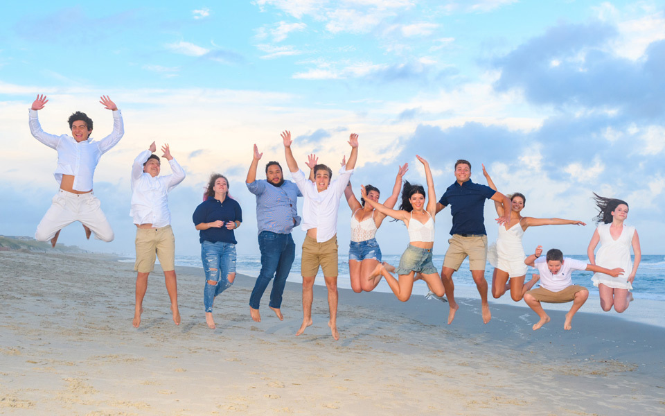 Eleven people jump, hands in the air, on a Hatteras Island beach under blue skies